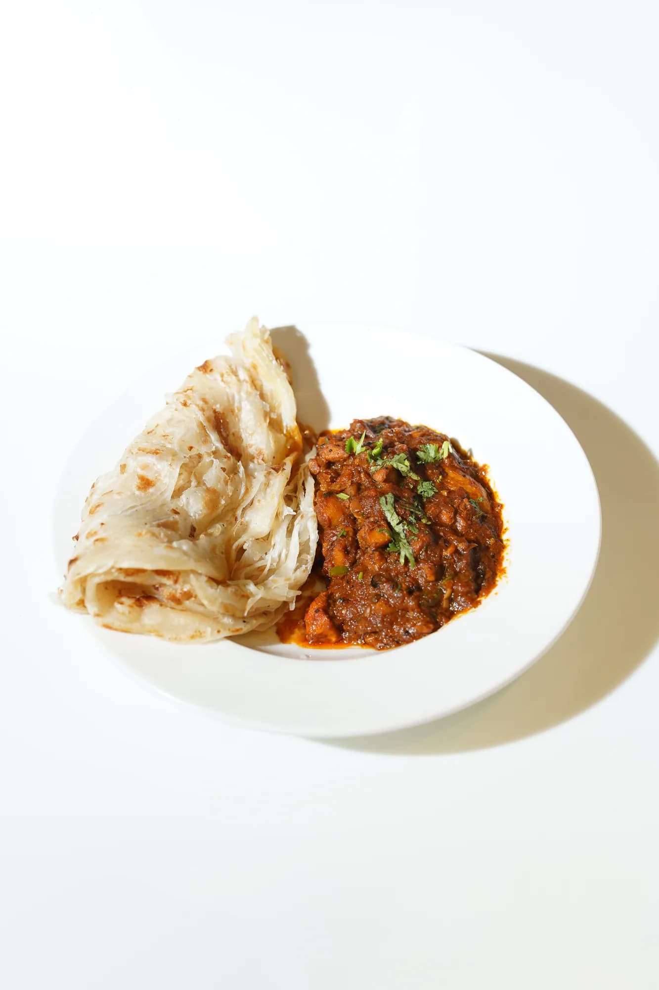 Layered parotta served beside a rich curry